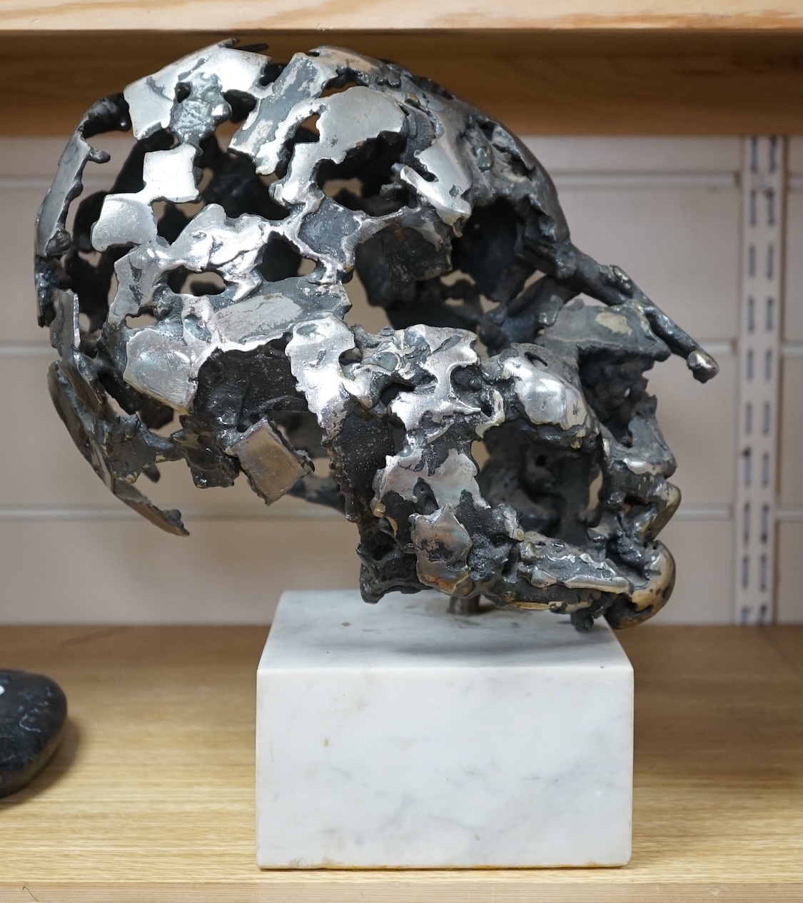 A modern polished steel skull, pierced and mounted on square white marble plinth, circa 1975, 31cm high. Condition - good, minor chipping